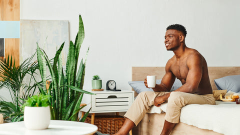 A healthy, well rested, muscular man sits on the edge of his bed ready to start the day. He's taken the best nighttime muscle recovery supplement