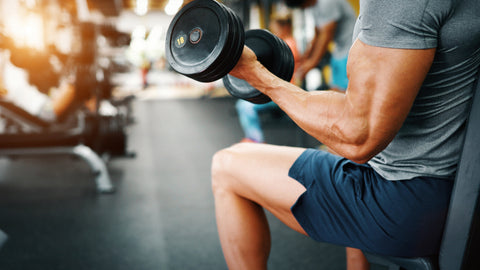 Creatine and Pre-Workout: Can You Take Them Together? A muscular arm is holding a dumb bell in a gym.