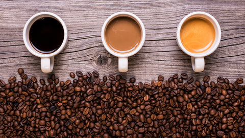 Caffeine Pills vs Coffee: Which is Best? 3 cups of coffee sit on a wooden backdrop with coffee beans scattered underneath.