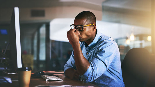 Can vitamins give you a headache? A man is sitting at his desk working and holding his forehead due to the pain of his headache.