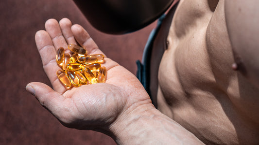 How much Omega-3 per day for bodybuilding? A bodybuilder is holding a palmful of clear omega-3 softgels that sparkle in the sunlight.