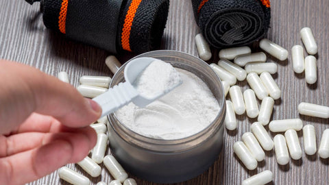 ow often should I take creatine? A hand holding a scoop of creatine above a tub of creatine surrounded by creatine capsules. 