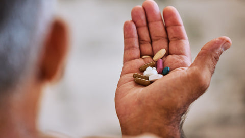 An older man with his hand held out. In the palm of his hand are colourful pill capsules representing the perfect vitamin B12 dosage for seniors