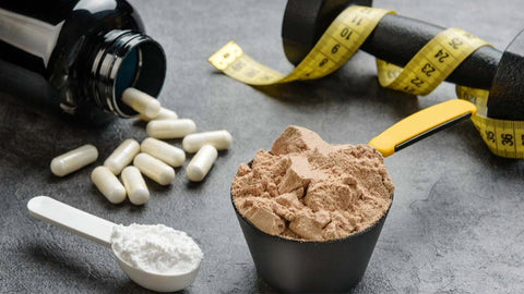 Scoops of creatine supplements along with capsules spilling out from a bottle with dumbells in the background and a tape measure. Mixing BCAA and creatine: A Good Idea?