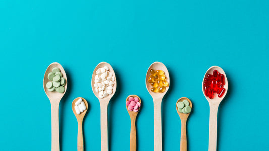 Multivitamin vs Individual Vitamins - What Is The Best Option? 7 wooden spoons are laid against a turquoise blue background. Each spoon holds a different type of brightly colored dietary supplement.