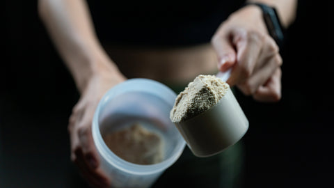 Close up of a person adding another scoop to their pre-workout shake. Conveying the point that taking too much pre workout isn’t a good thing and there are reasons to limit your dose.